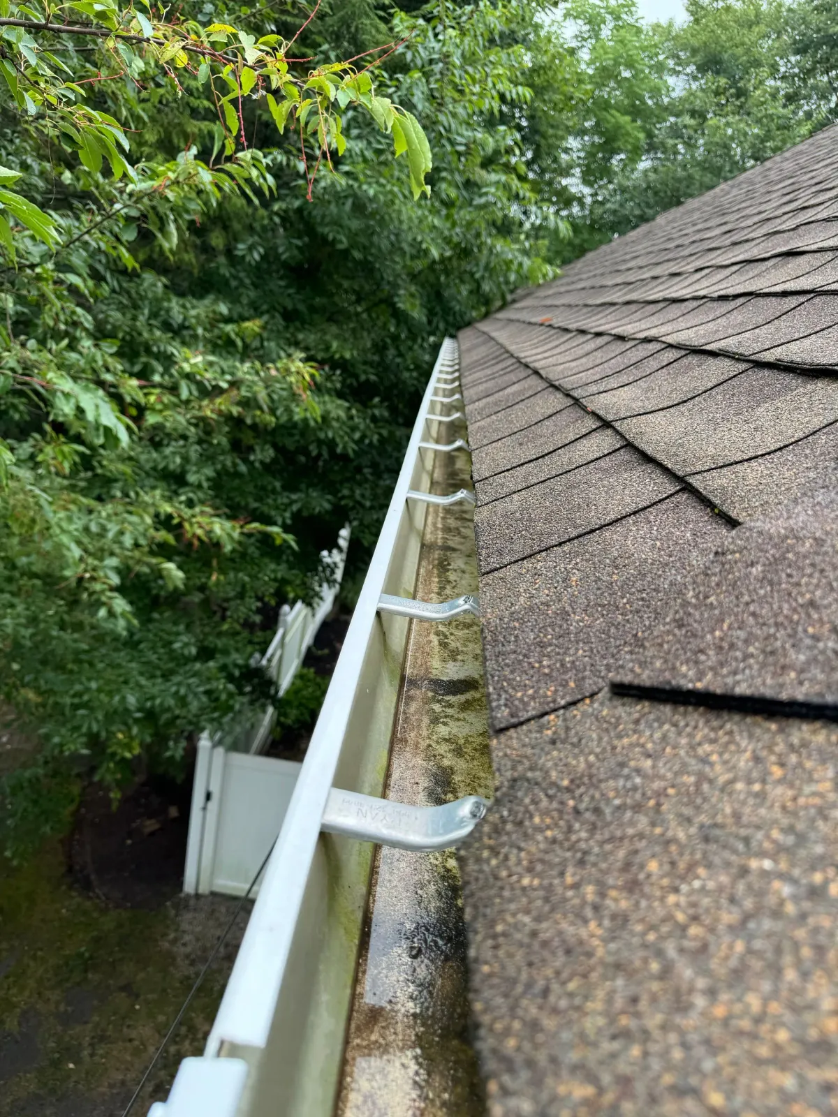 A close up of a gutter on a roof with trees in the background.