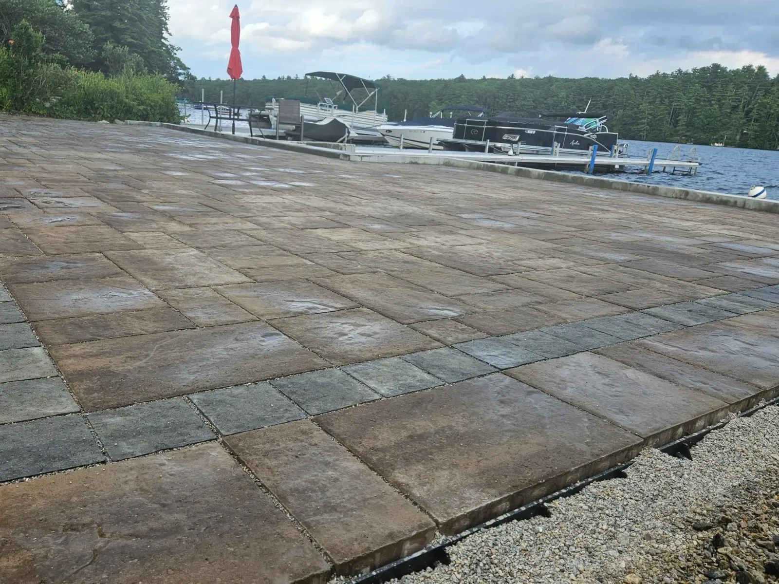 Paver patio near a lake with boats docked and a wooded shoreline in the background.