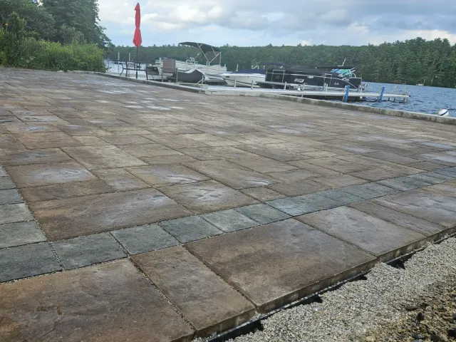 Paver patio near a lake with boats docked and a wooded shoreline in the background.
