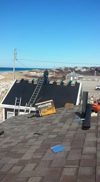 Roofer on a ladder installing shingles on a house roof near the beach on a sunny day.