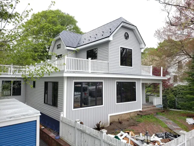 Modern gray two-story house renovation featuring white siding, a rooftop deck, and new black frame windows.