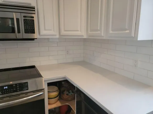 Empty white kitchen corner with stainless stove, microwave, and open cabinet under quartz countertop