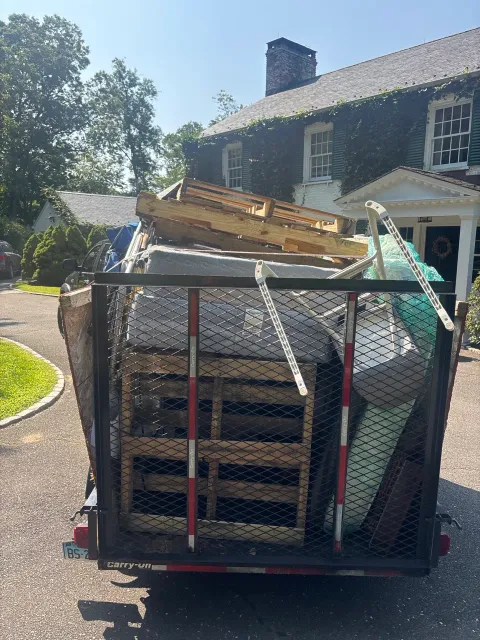 Utility trailer loaded with mattresses, wood and household items in a driveway