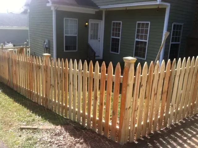 A wooden picket fence is in front of a green house.