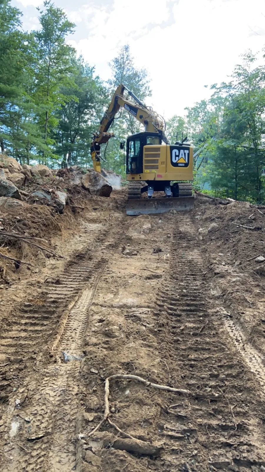 CAT excavator cutting new driveway down steep wooded hillside, Monson MA
