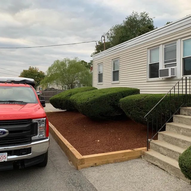 Timber-edged mulch bed and trimmed shrubs along a ranch front