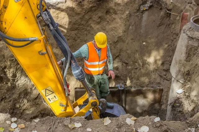 Worker in hard hat and safety vest working in an excavated area with excavator.