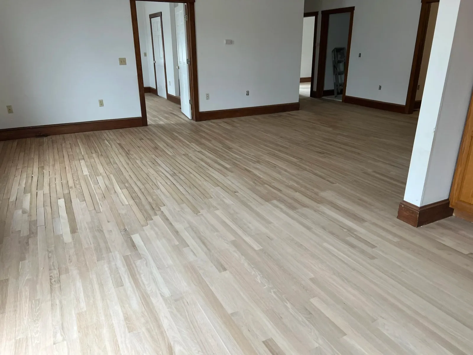 Empty room with light wood flooring and white walls, with doorways leading to other rooms.