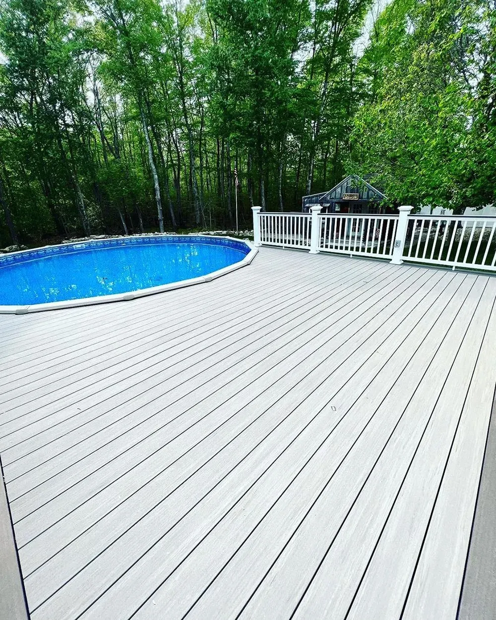 A large wooden deck with a swimming pool in the background