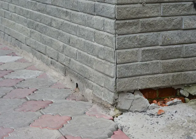 Brick wall corner with damaged base and paving stones.