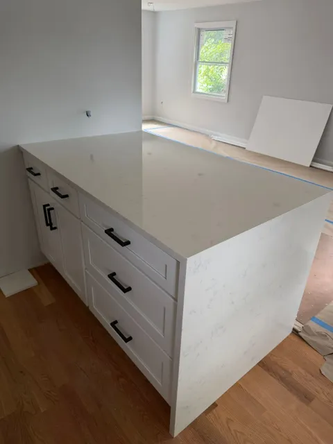 White kitchen island with drawers in an unfinished room with wood floor and a small window.