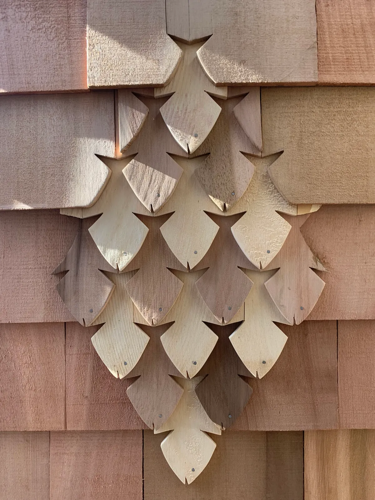 Close-up of a cluster of wood shingles shaped like pine cones on a house exterior.
