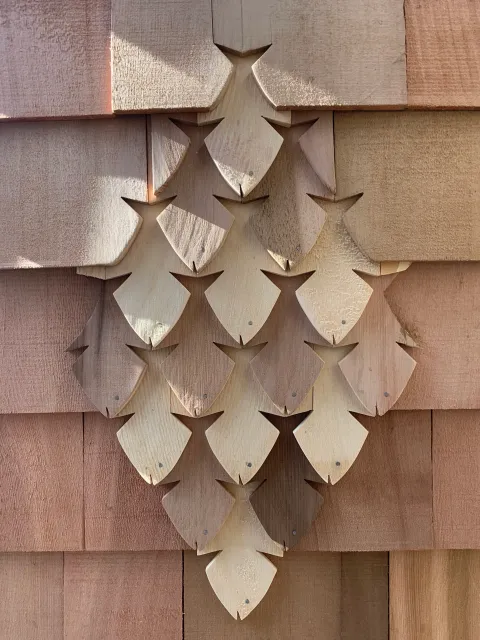 Close-up of a cluster of wood shingles shaped like pine cones on a house exterior.