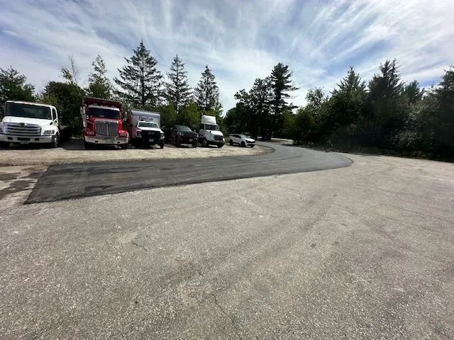 Parking lot with several trucks and cars parked along a tree-lined edge under a cloudy sky