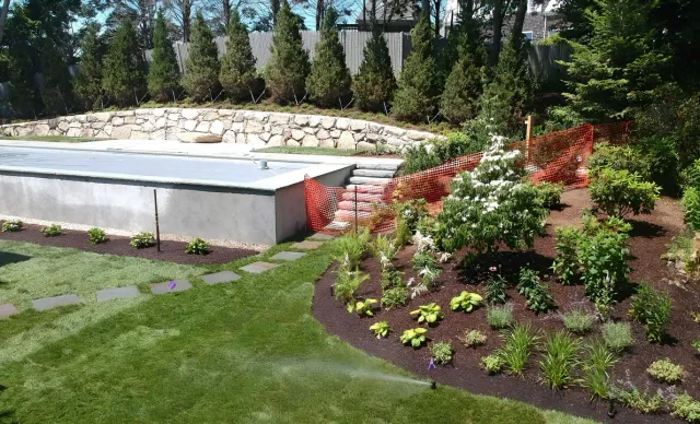 Landscaped garden with flower beds, shrubs, and a stone wall beside a concrete patio
