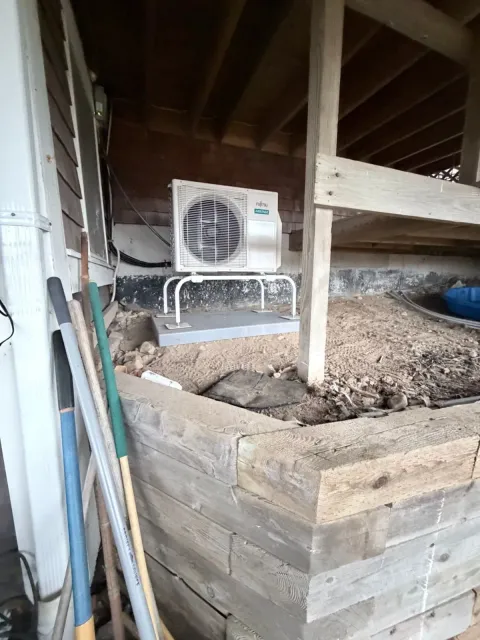 Air conditioner mounted in a cluttered attic or crawl space with wooden beams and soil piles