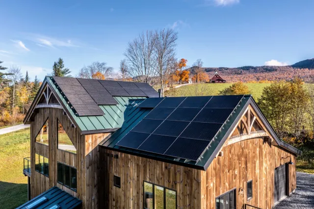Timber home with weathered wood siding, gabled roofs and a meadow beneath autumn hills.