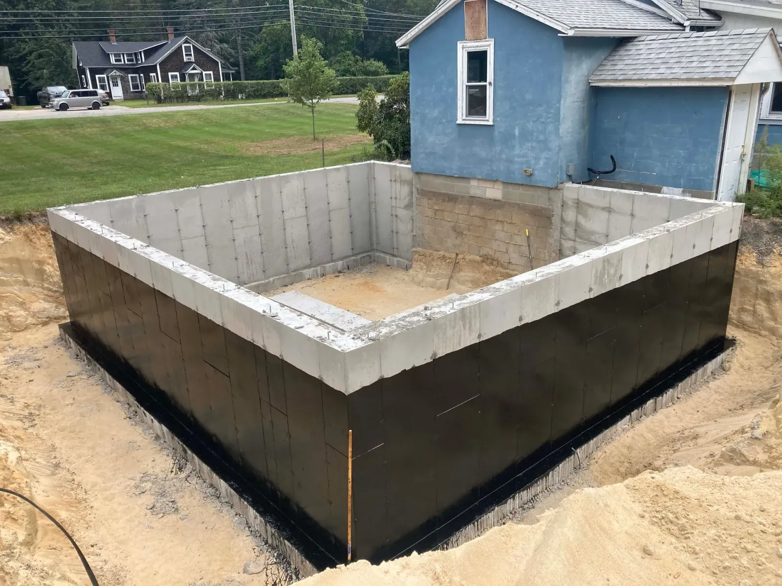 A large concrete wall is being built in front of a blue house.