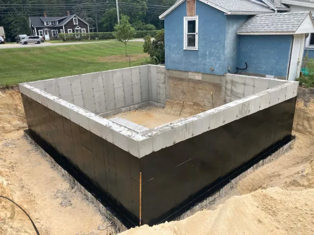 A large concrete wall is being built in front of a blue house.