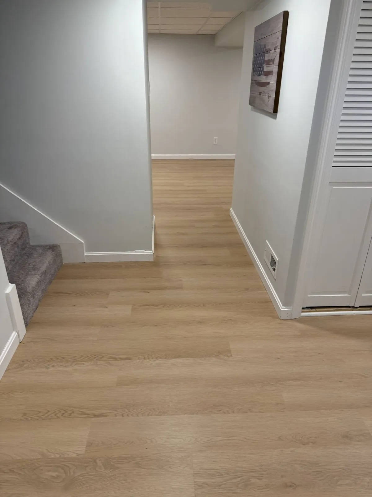 A hallway with hardwood floors and stairs in a basement.