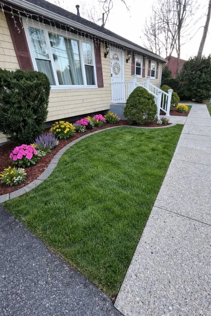 Suburban home with cream and burgundy siding, manicured lawn, colorful flower beds with pink and yellow blooms, and concrete driveway