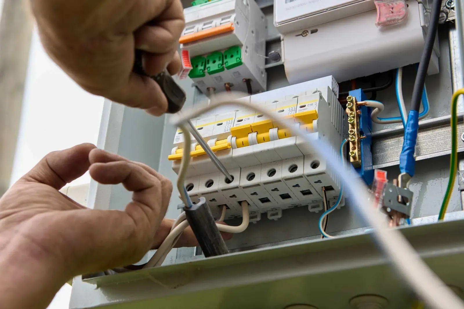 Electrician working on electrical panel with a screwdriver.