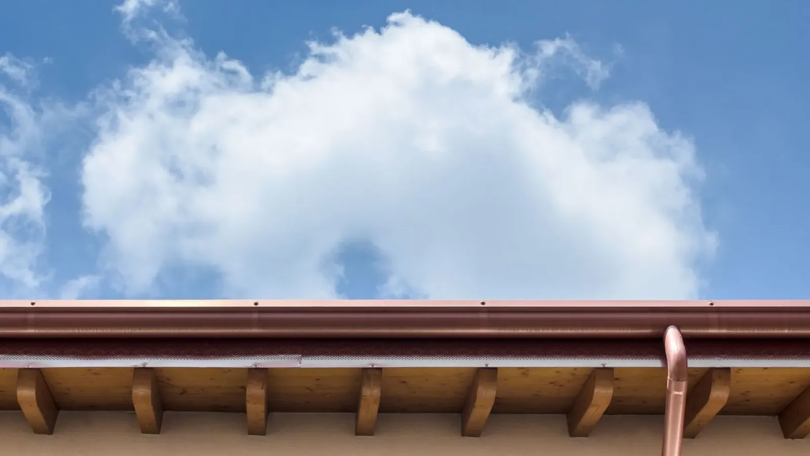 A roof with a gutter and a blue sky with clouds in the background.