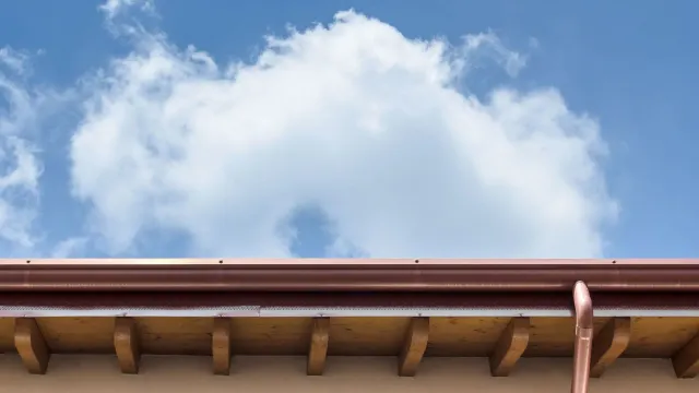 A roof with a gutter and a blue sky with clouds in the background.