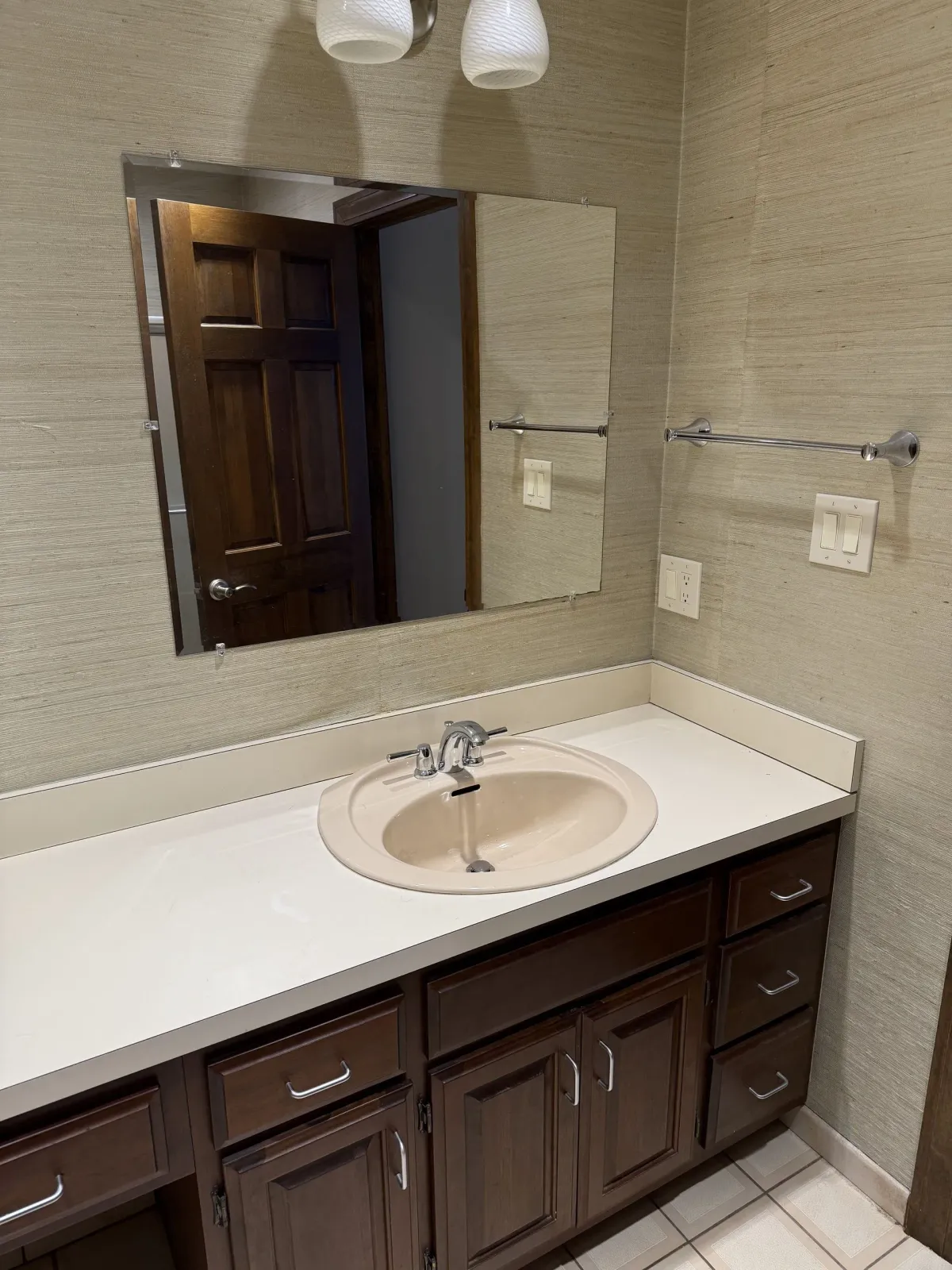 Bathroom with dark wood vanity, light-colored countertop, and a beige sink. Mirror and wall-mounted towel rack.