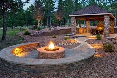 A fire pit in a backyard with a gazebo in the background.