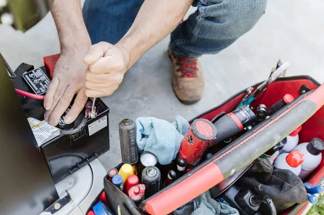 Man installing a generator battery with tools from a red tool bag.
