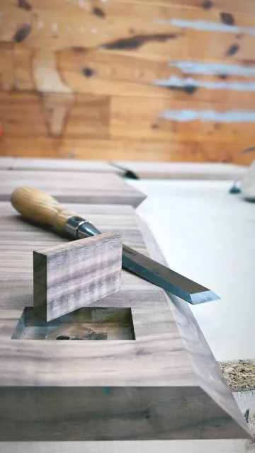 A woodworking workbench with a hand plane, carving chisel, and a piece of wood.