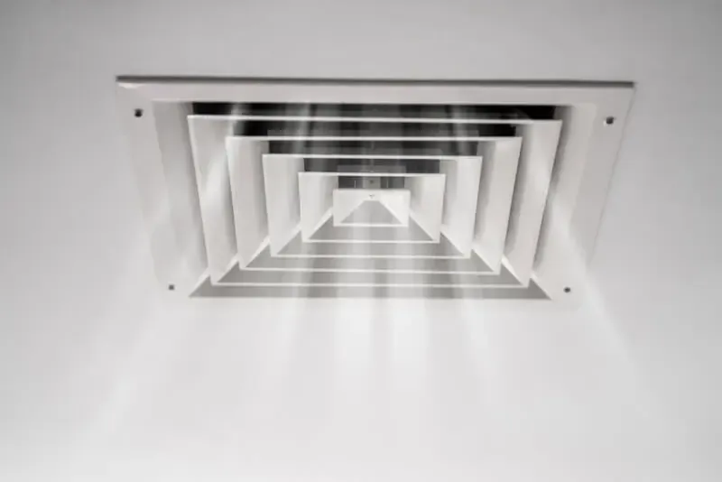 White ceiling air vent with layered rectangular slats seen from below, creating a tunnel effect.