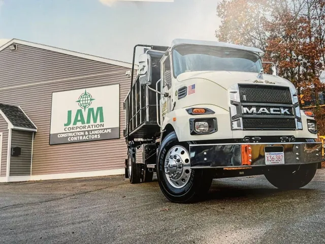 A large Mack Dump Truck is parked in front of the building and sign for JAM Corporation in Worcester, MA.