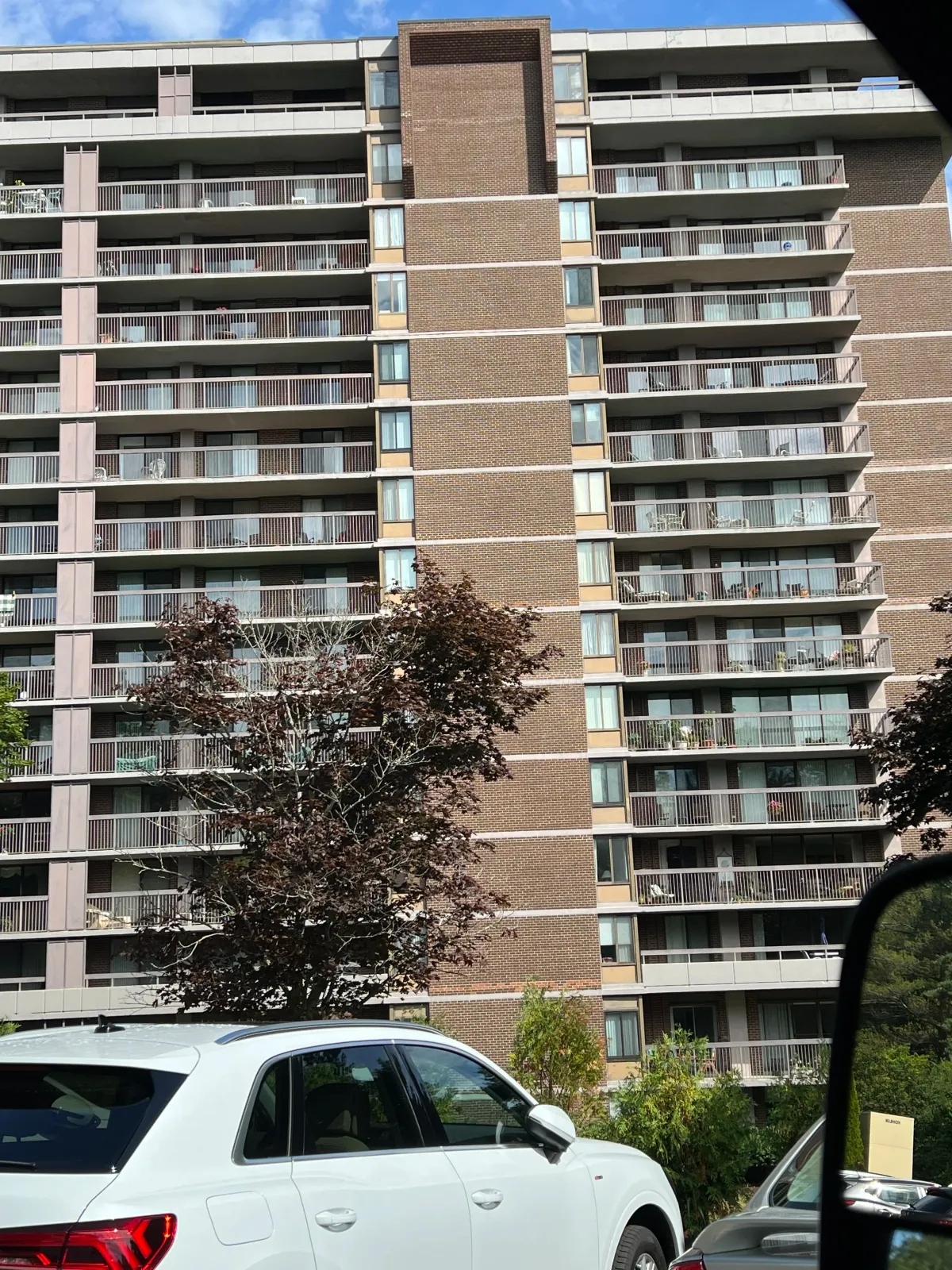 High-rise apartment building with balconies, parked white SUV in foreground.