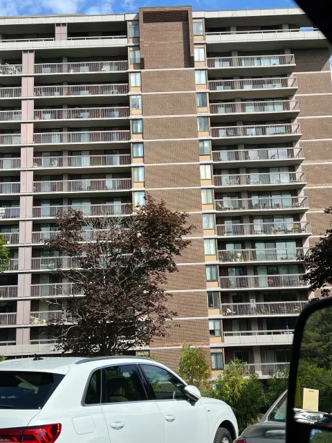 High-rise apartment building with balconies, parked white SUV in foreground.