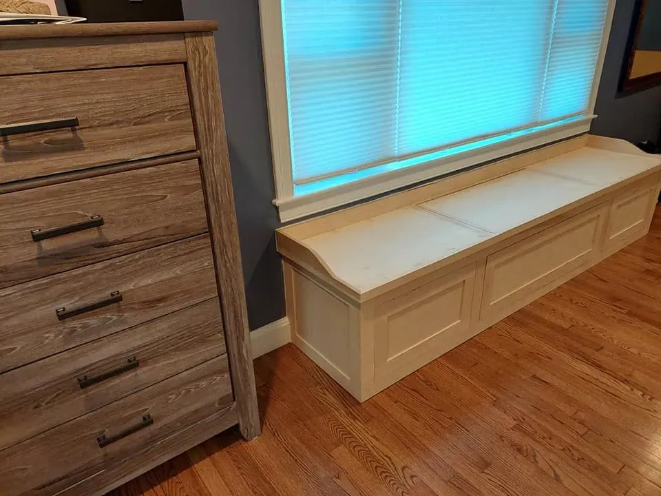 Window seat with dark cabinets, two boxes, and a plant beside a large window.