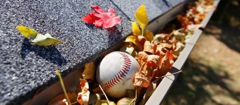 A baseball sits in the gutter of a home.