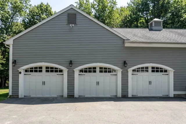 Gray three-car garage with white doors and siding, surrounded by trees on a sunny day
