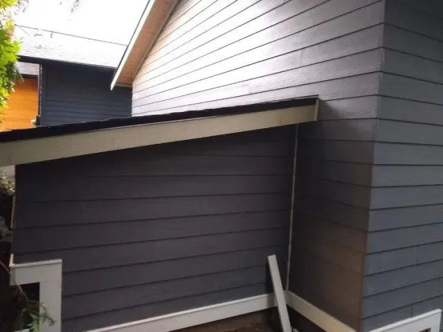 Dark gray house siding and slanted roof over a narrow exterior walkway.