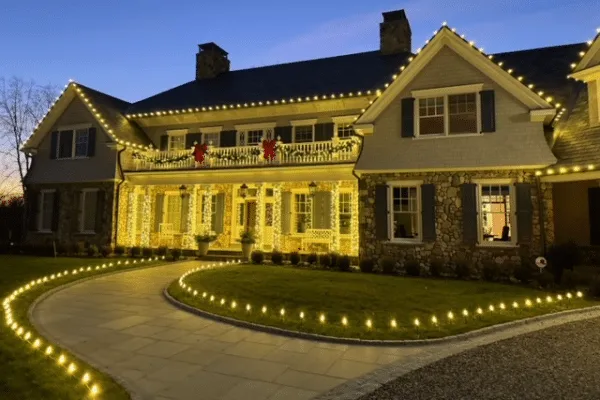 Elegant home illuminated with landscape lighting, highlighting the architecture and walkway. Warm white lights line the roof, porch, and path, creating a welcoming and festive atmosphere.