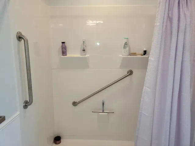 Accessible shower stall with grab bars, shower bench, and curtain in a white tiled bathroom