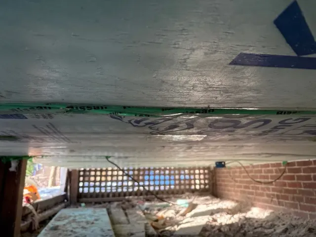 Under a low concrete floor, a brick wall and debris are visible in a cramped crawlspace.