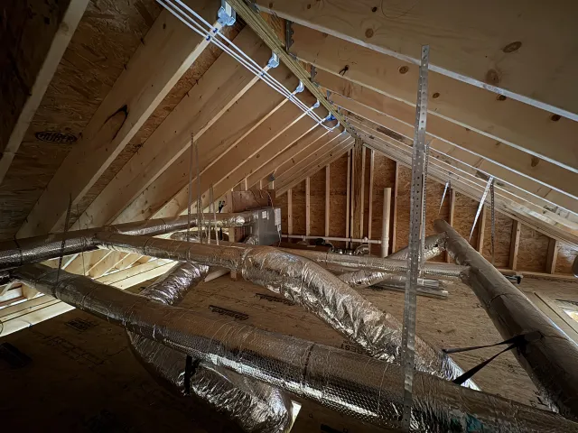 Insulated HVAC ducts installed in an unfinished attic with exposed wooden roof framing.