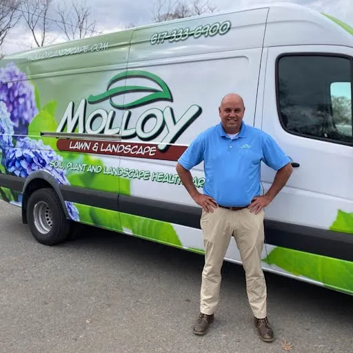 Molloy Landscape lawn care expert standing by branded service van, providing professional lawn and landscape services in Milton, MA.