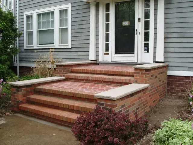 Brick front steps leading to a gray house with white trim and a black front door
