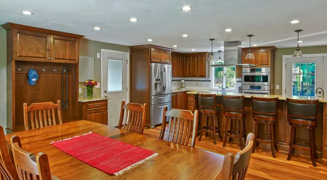 Spacious kitchen with wood cabinets, island bar stools, and a wooden dining table with a red runner.