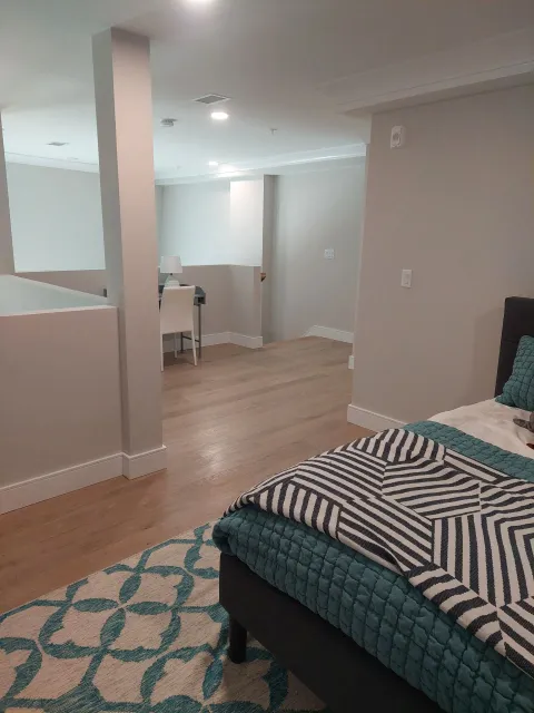 Bedroom with hardwood floors and teal rug; bed with striped throw blanket; view into hallway.