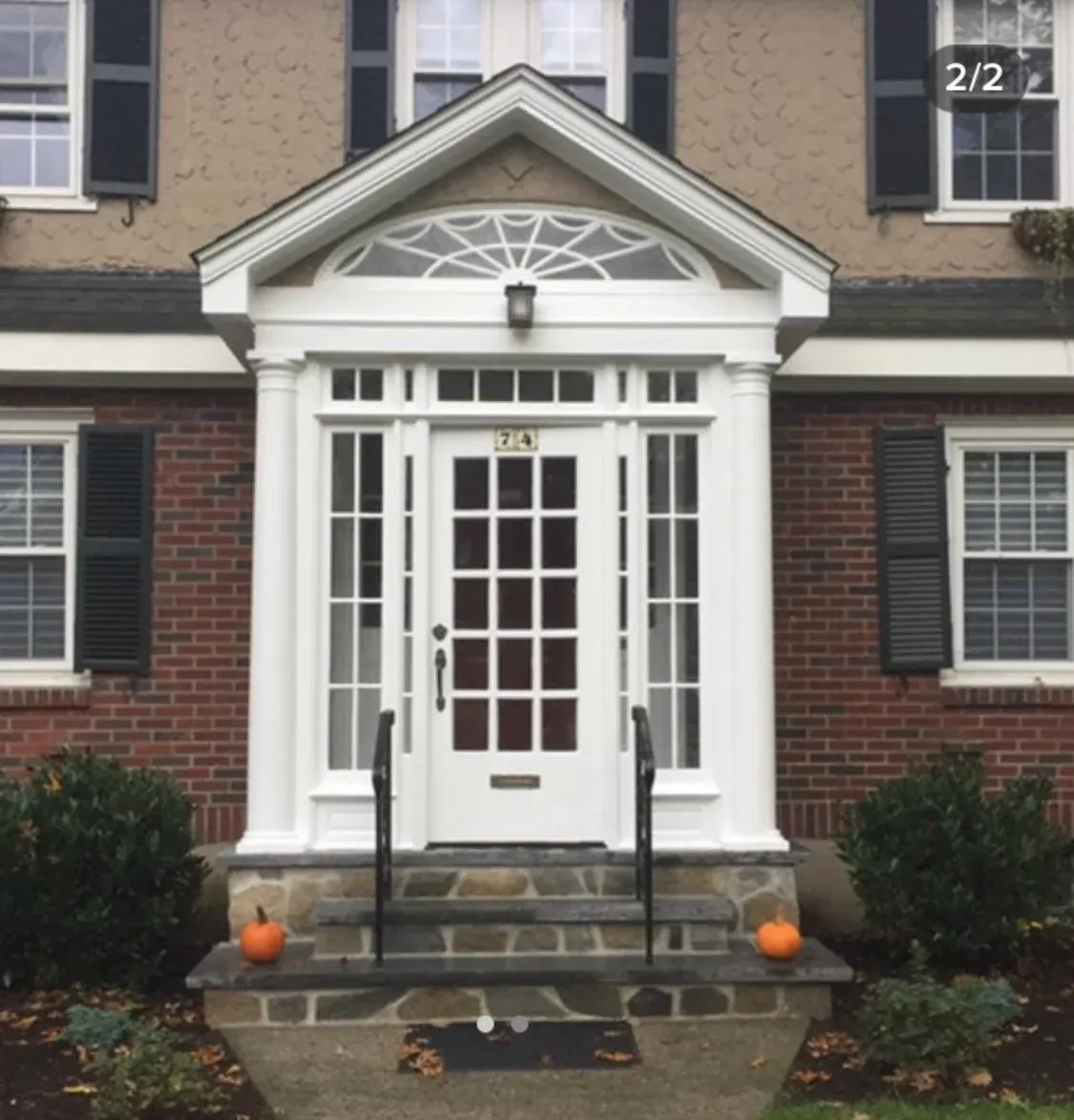 Front entrance of a house with white columns, a glass door, and two small pumpkins on the stone steps.