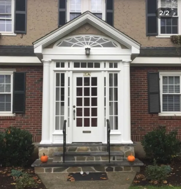 Front entrance of a house with white columns, a glass door, and two small pumpkins on the stone steps.